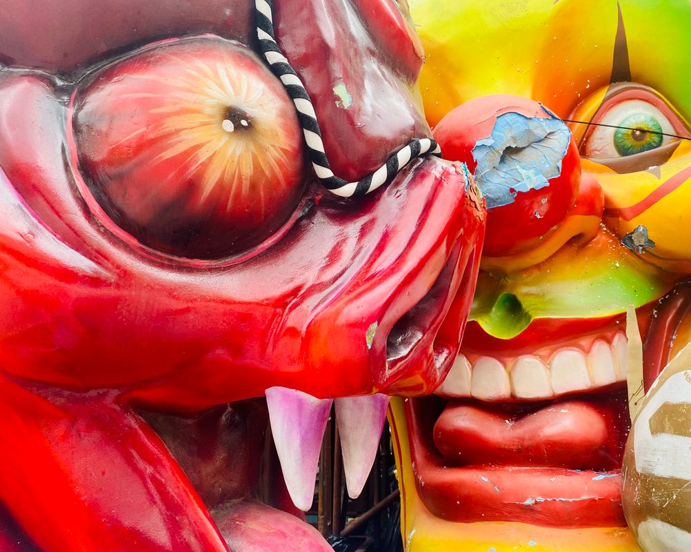 Close-up van kleurrijke, beschadigde carnavalsmaskers waarin een rood monsterfiguur en een felgezicht met kapotte neus te zien zijn.