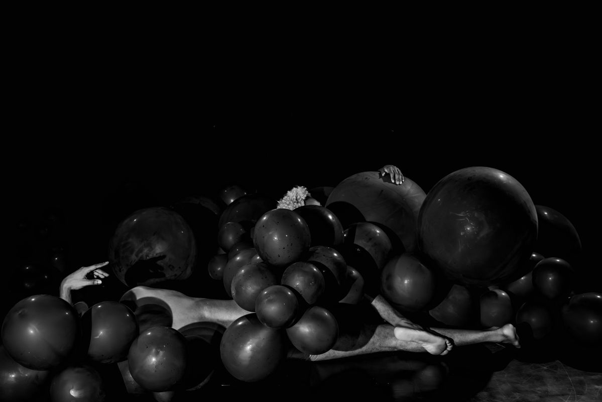 Twee dansers liggen op de grond, bedolven onder zwarte balonnen.