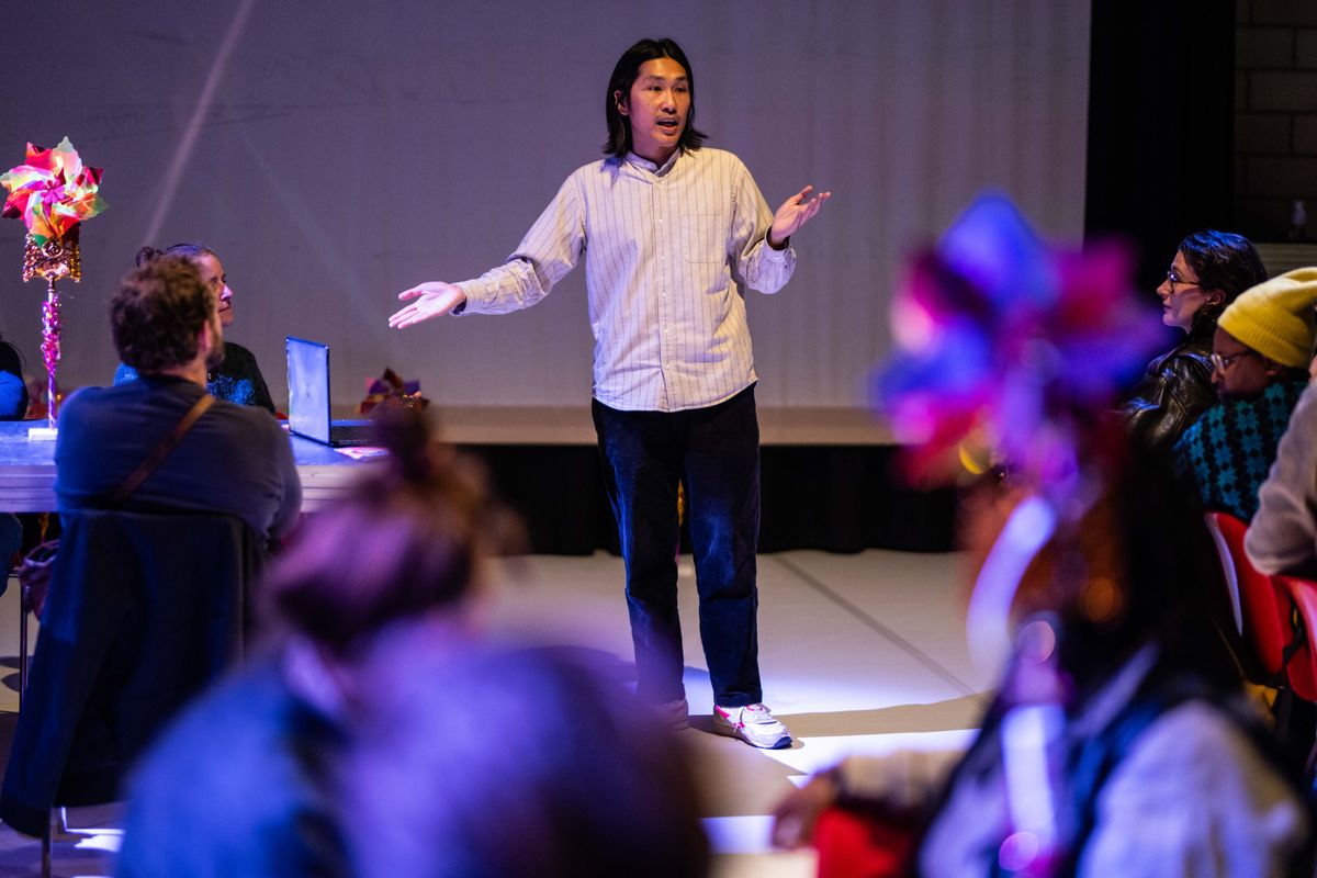 Een spreker staat midden in de ruimte en richt zich tot een publiek dat om hem heen zit.