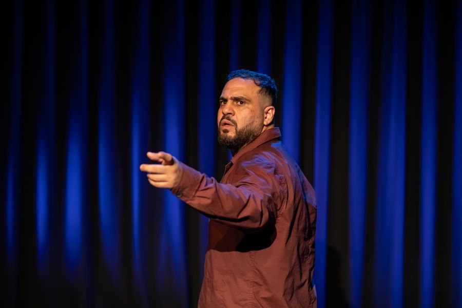 Man met kort baardje van opzij, bordeauxkleurig overhemd, donkerblauwe achtergrond