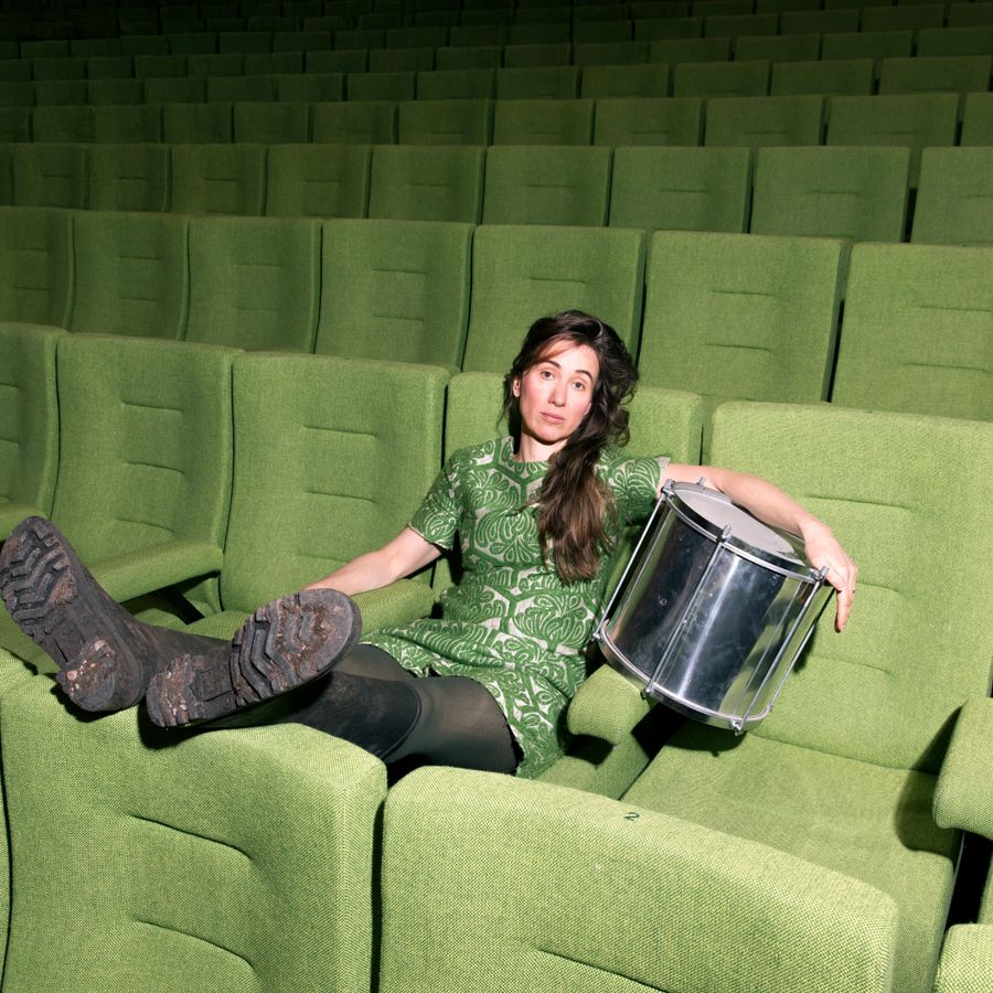 Dame in groene theaterstoel met floortom onder haar armen. 