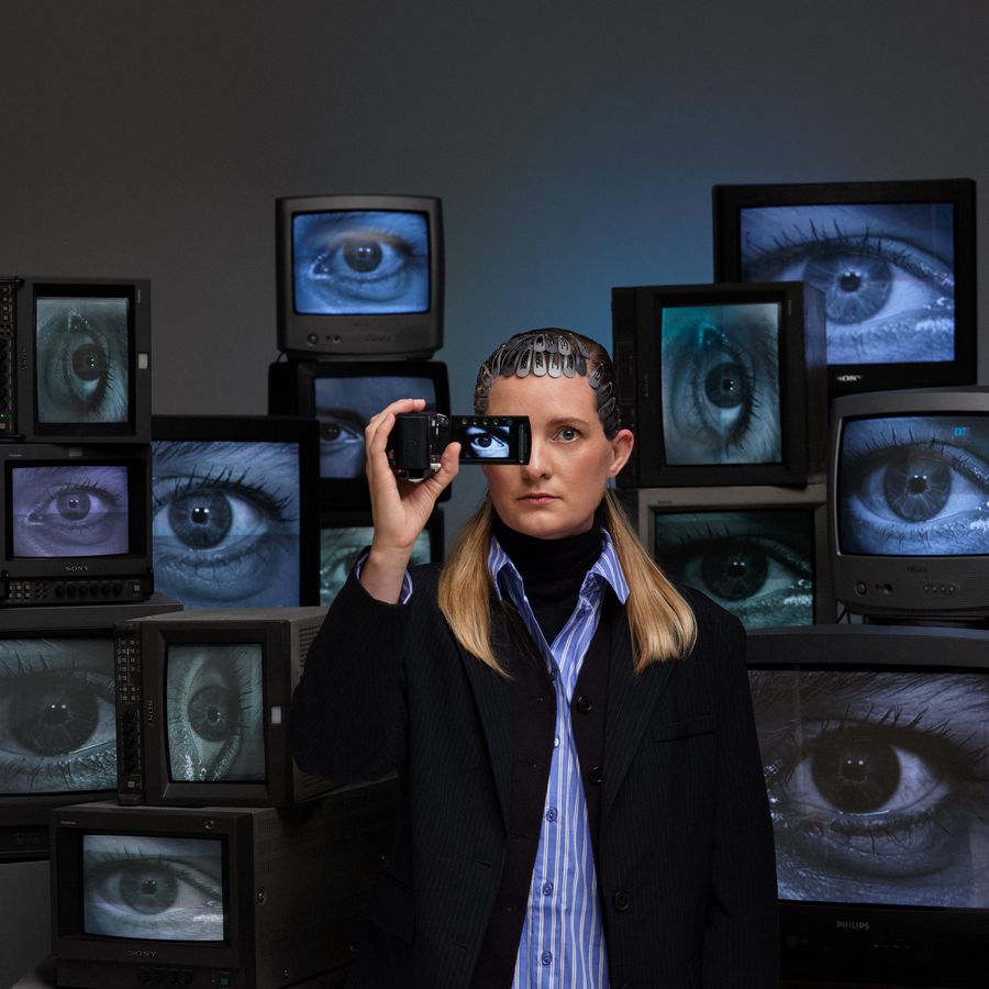 Donna met een camera voor 1 oog en 10 tv schermen achter zich