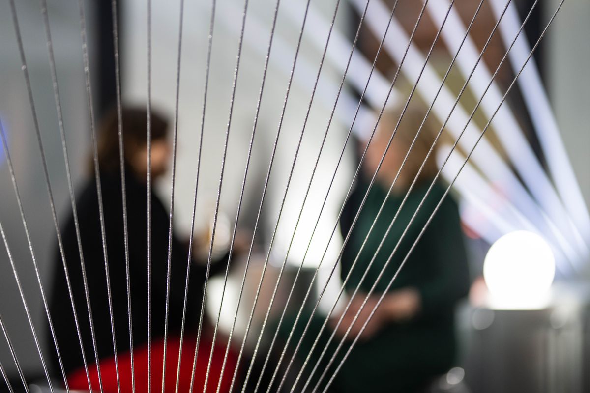 Twee personen praten achter een web van gespannen draden, waardoor het beeld abstract en diffuus wordt.