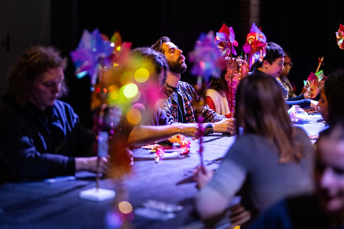 Bezoekers zitten aan een lange tafel omgeven door kleurrijke, fonkelende molentjes.
